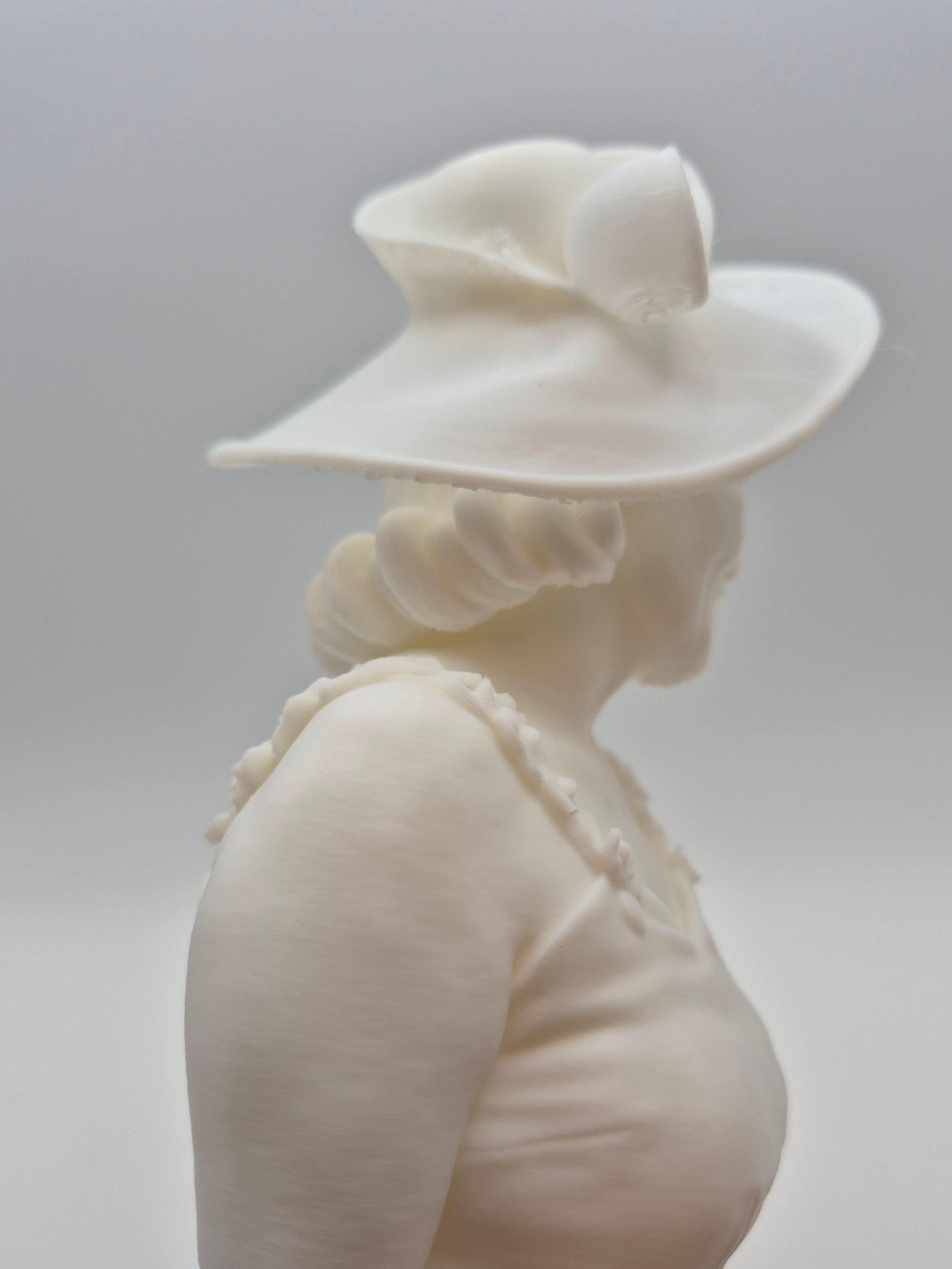 White ceramic sculpture of a person wearing a hat on a plain background